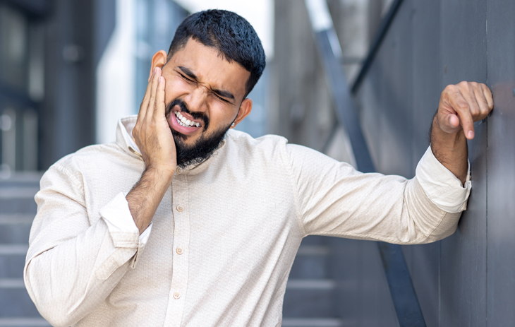 Smiling male dentist in white coat gestures welcomingly in modern dental office setting.