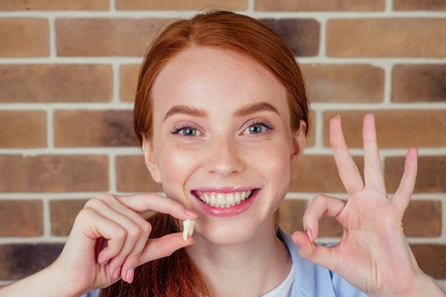 Smiling young woman with red hair pointing to her teeth against brick wall background.