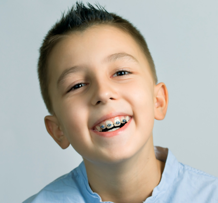 Young boy smiling brightly against neutral background for dental practice portrait.