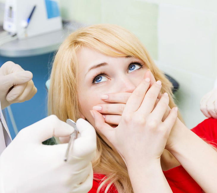 Anxious female patient in dental chair looking worried during examination at dentist office.