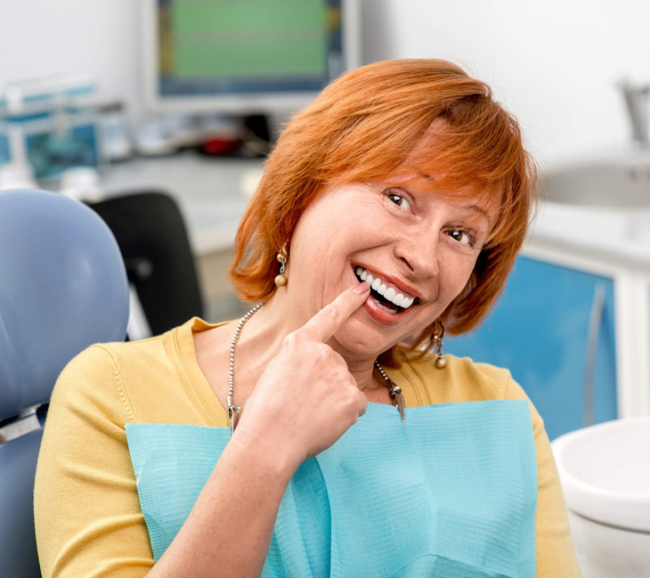 Woman in yellow shirt smiling at dental office with computer equipment visible in background.