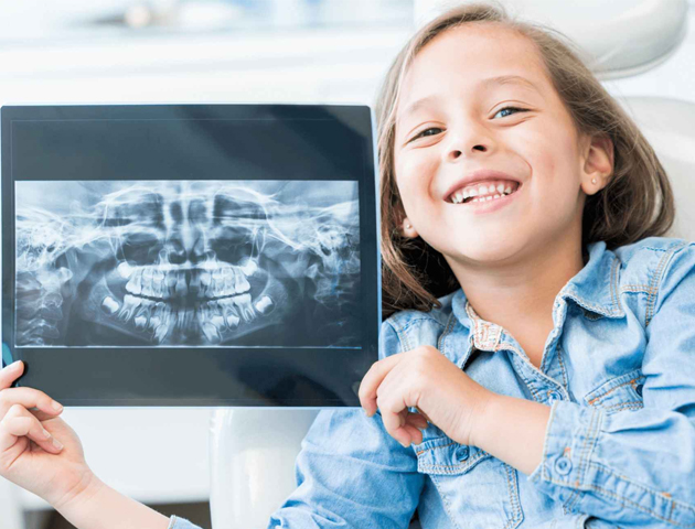 Young girl smiling while holding dental X-ray in clinical setting at Austin Park Dental.
