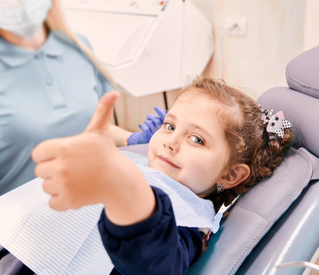 Young child giving thumbs up in dental chair during examination at Austin Park Dental.
