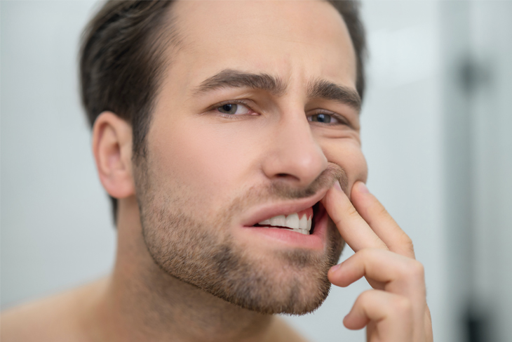 Man touching his mouth experiencing tooth pain or dental discomfort indoors.