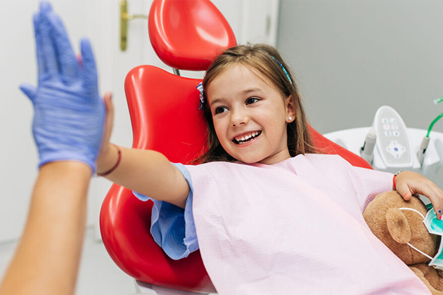 Young child wearing boxing gloves giving high-five to dentist in dental office setting.
