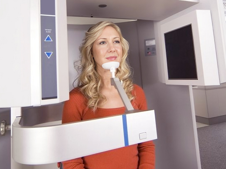 Woman in orange top holding dental model in modern dental office treatment room.