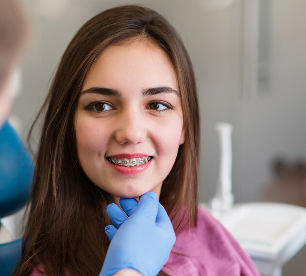 Young female patient smiling in dental office wearing pink bib, dentist in blue gloves.