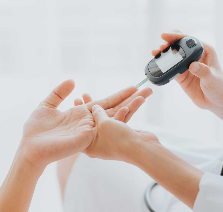 Person performing blood glucose test with finger prick device on white background.