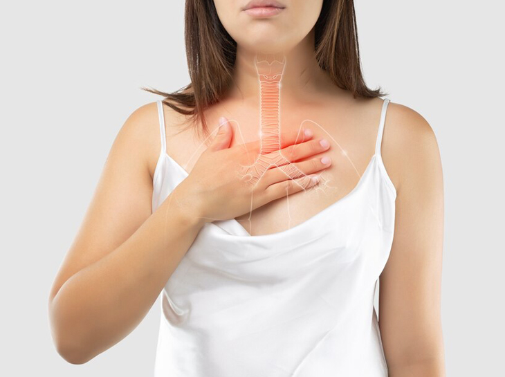 Woman in white tank top holding chest, experiencing heartburn or acid reflux discomfort.