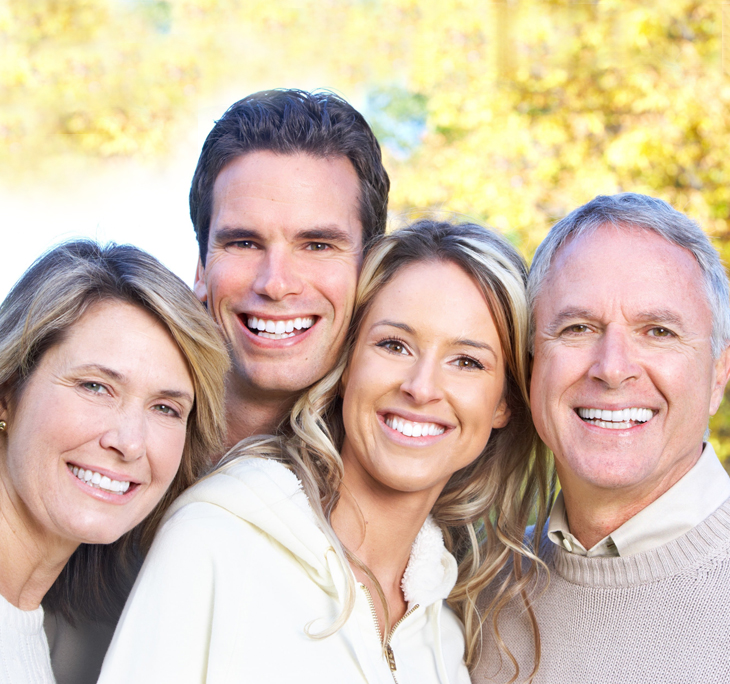Four smiling people posing together outdoors with warm, golden sunlight in background.