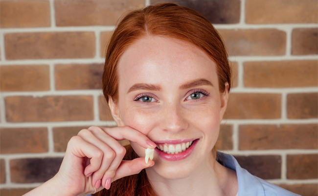 Smiling young woman with red hair against brick wall, resting chin on hand.