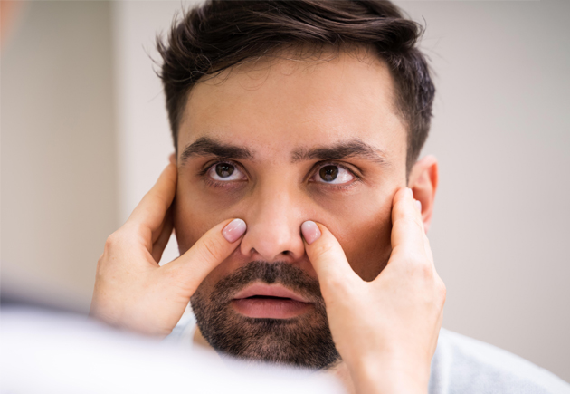 Man examining his nose and sinuses with concerned expression in clinical setting.