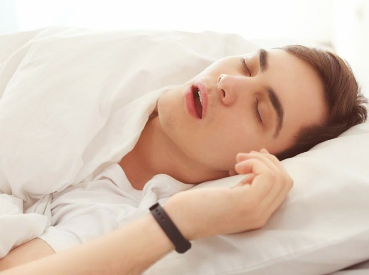 Person sleeping peacefully in bed wearing white bedding and a smartwatch.