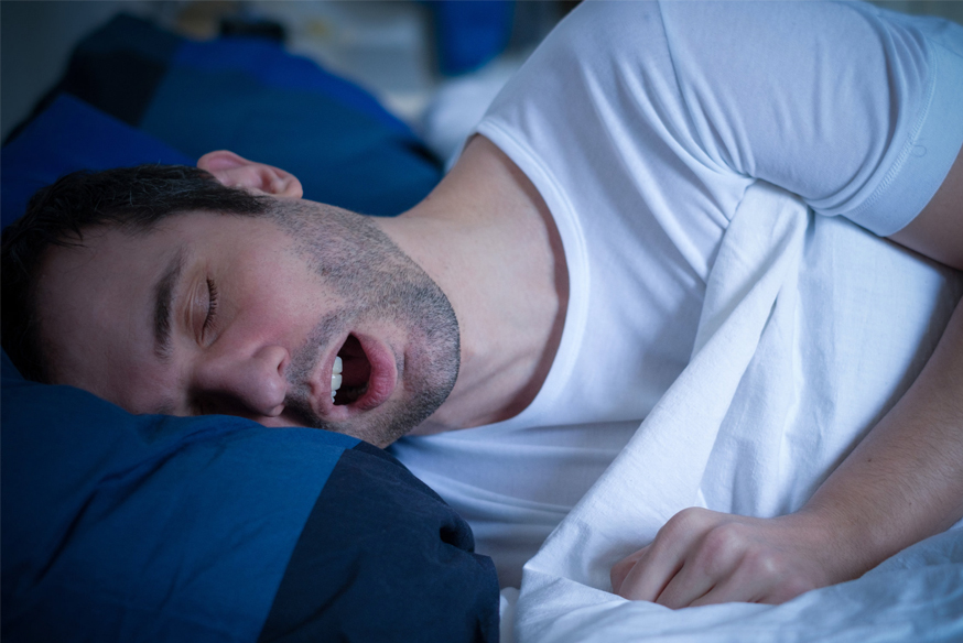 Man sleeping on blue pillow in white shirt, mouth open.
