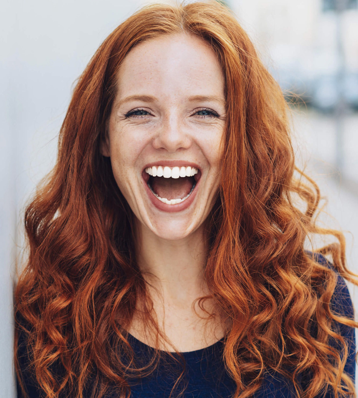 Woman with red wavy hair smiling brightly in dental office setting.