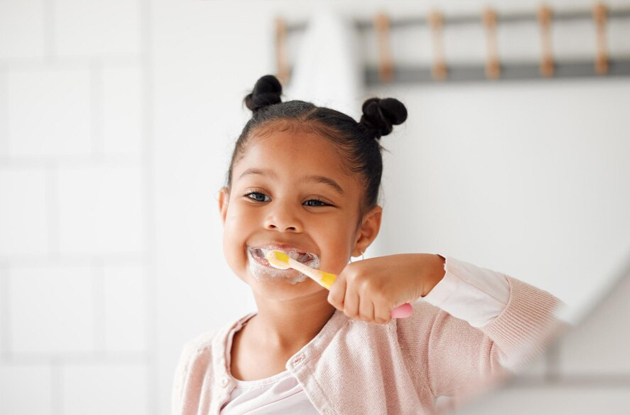 Young child brushing teeth with pink toothbrush in bright bathroom setting.