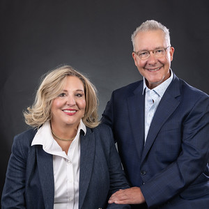 Two dental professionals in business attire posing together against a dark background.