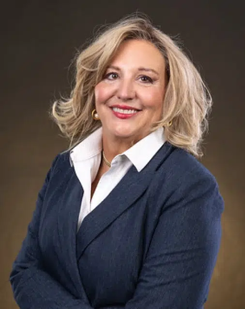 Professional woman in dark blazer smiling at camera, dental office portrait photo.